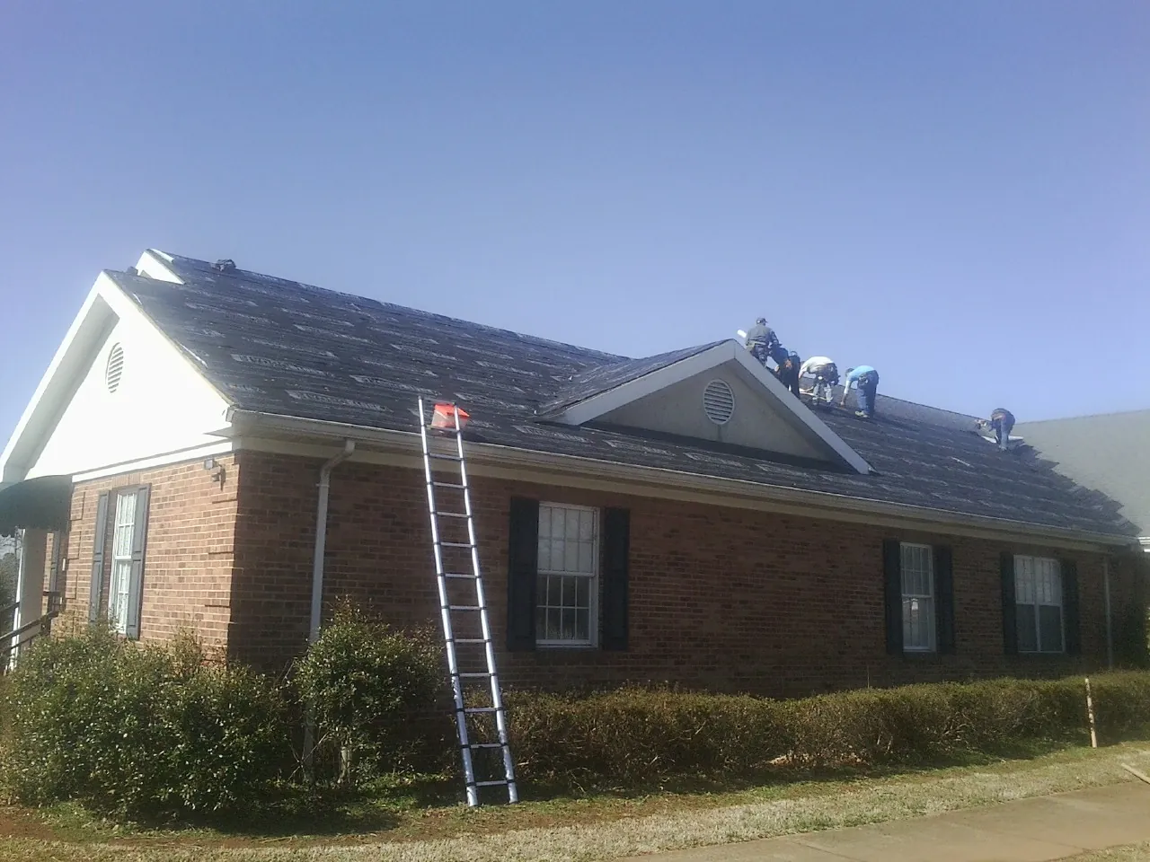 Crew tearing shingles off a brick ranch roof with a ladder set — Emergency Roof Repair work by our crew in Elrama