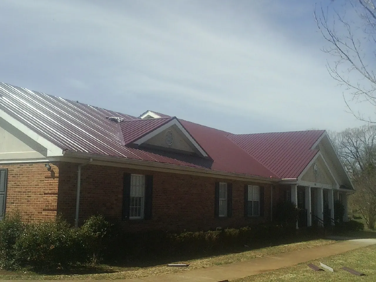 Red metal roof with gabled entries on a long brick building, from a Hail Damage Roof Repair job in Elrama