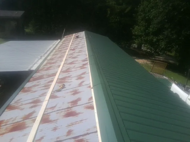 Old rusted panels beside newly installed green metal roofing — Wind Damage Roof Repair by Roofing Brothers in Elrama