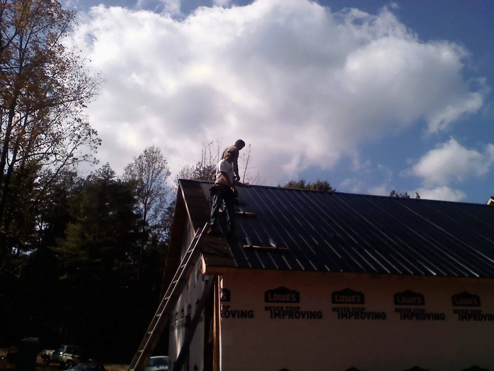 Roofer fastening dark metal panels high against a cloudy sky, from a Roof Inspection job in Elrama