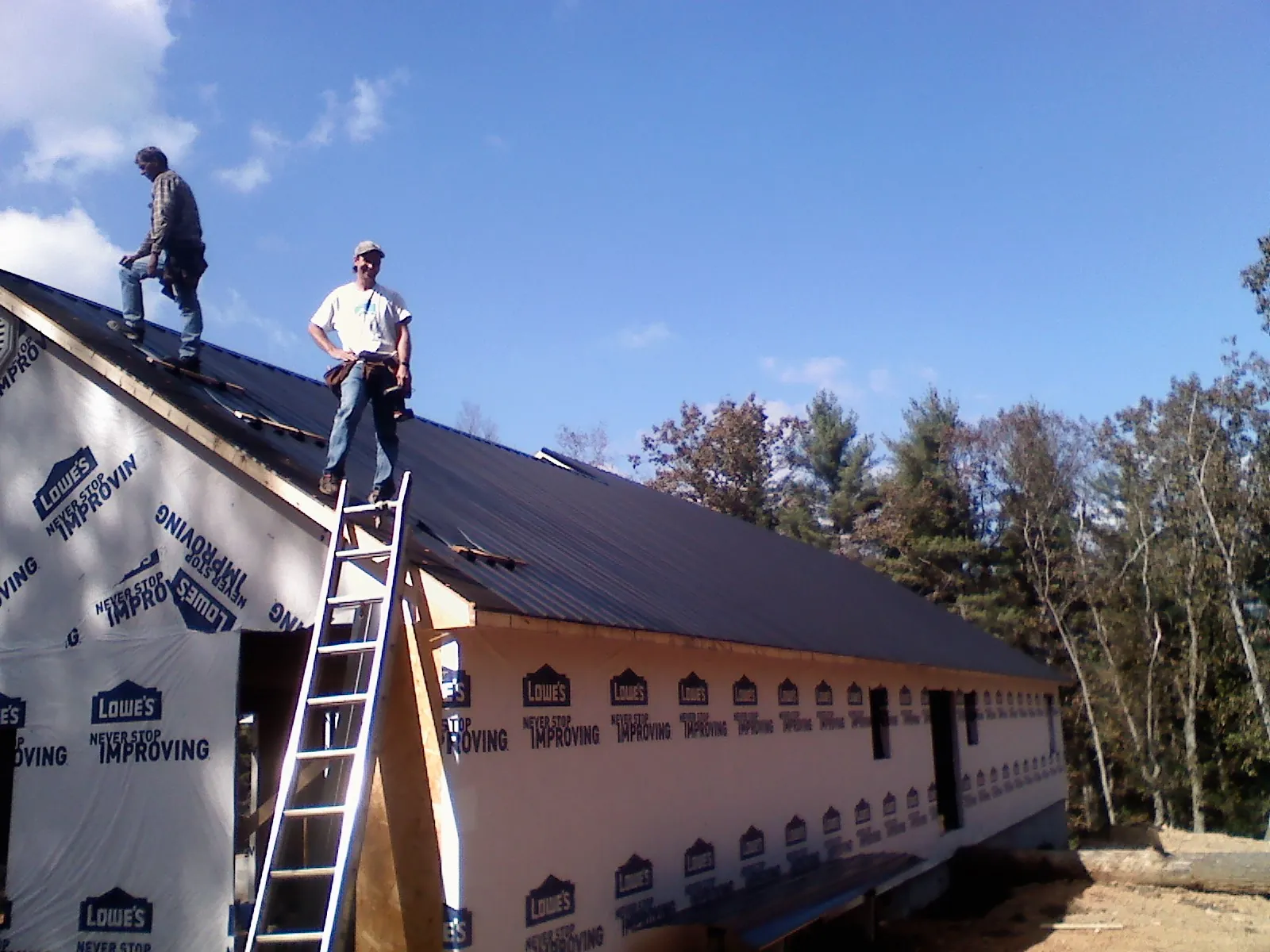 Two roofers standing on a long dark metal roof over a wrapped building in Elrama