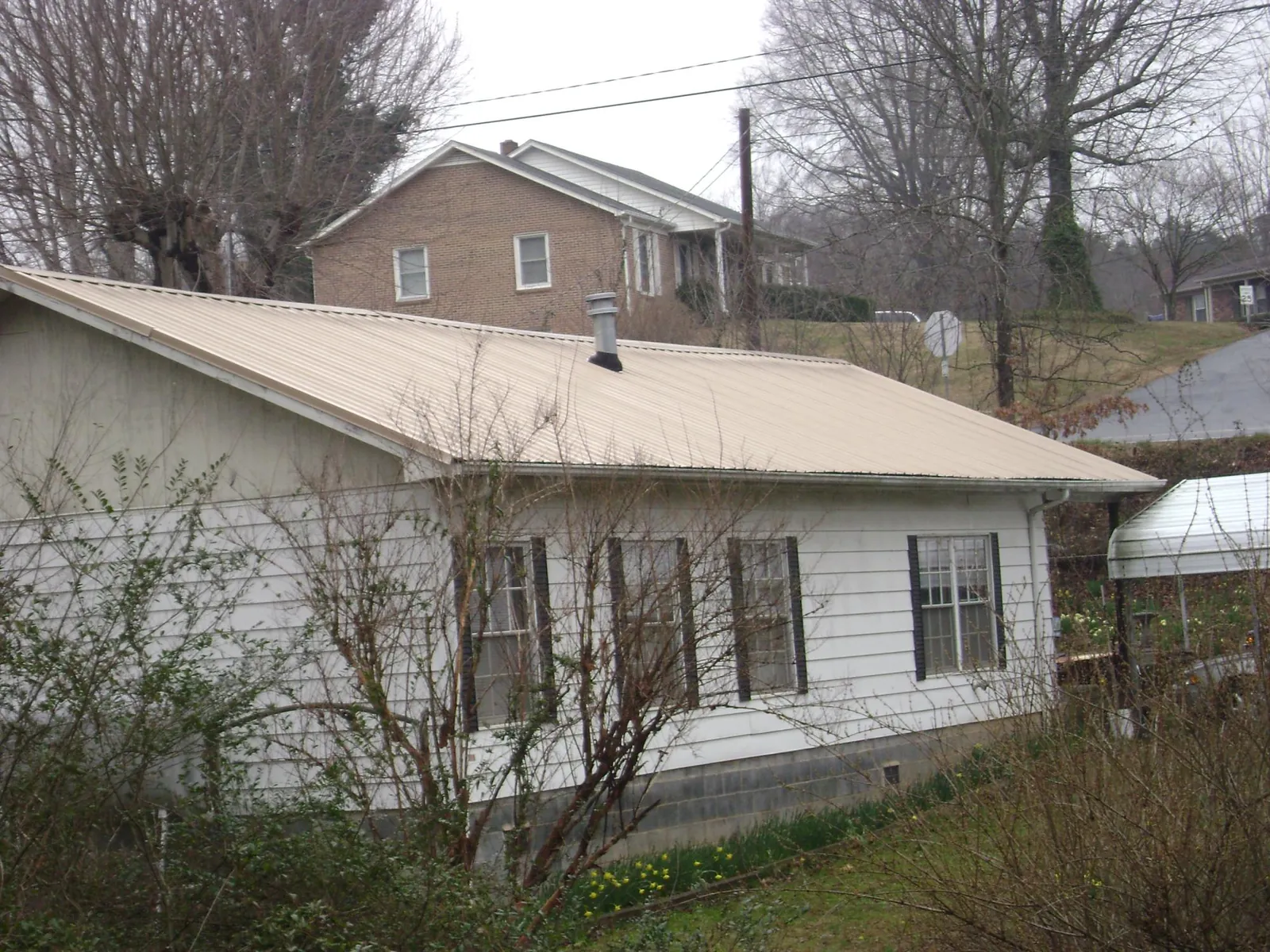 Tan metal roof on a white sided house set into a hillside — Commercial Roofing by Roofing Brothers in Elrama